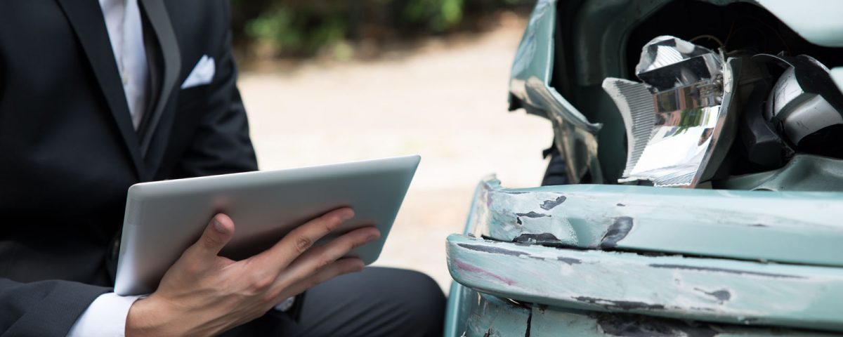 Person inspecting a damaged car with a tablet after an accident.